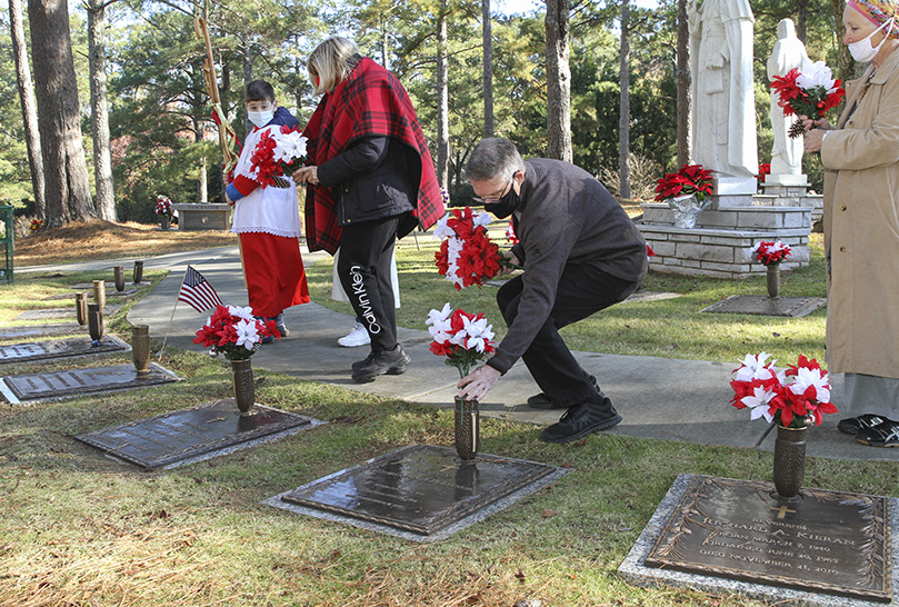 Jim O’Connor of Holy Spirit Church, Atlanta, squatting, places an arrangement of artificial poinsettias on the grave of the late Father Edward O’Connor. Participants went to each grave of a priest and bishop in the Calvary section at Sandy Spring’s Arlington Memorial Park, as their names were called out. Father O’Connor, a priest for nearly 60 years, died in November of 2016. Photo By Michael Alexander