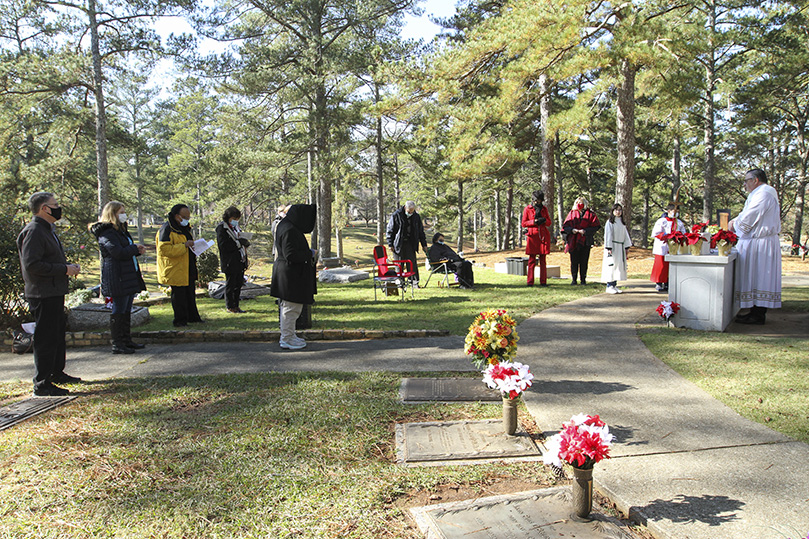 After the poinsettias were placed on the graves of the deceased clergy, the participants, including Deacon Jim Grebe of Holy Family Church, Marietta, far right, prayed the Glorious Mysteries of the rosary. Photo By Michael Alexander