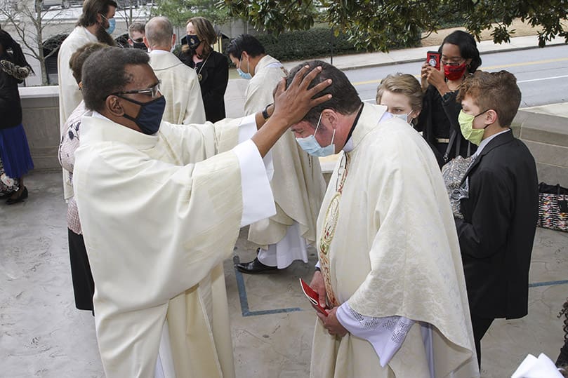 Out on the plaza at the Cathedral of Christ the King, Atlanta, newly ordained permanent deacon Carl Taylor, left, extends a blessing to Father Joseph Shaute, his pastor from St. Theresa of the Child Jesus Church in Douglasville. Photo By Michael Alexander