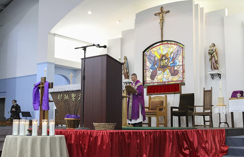 Father Bill Hao, background, the chaplain for the Chinese Catholic community, is the principal celebrant at the March 21 Mass. At the foot of the altar, eight candles were lit by parishioners to honor the eight victims killed in the March 16 mass shooting at three Atlanta-area massage parlors. Photo By Michael Alexander