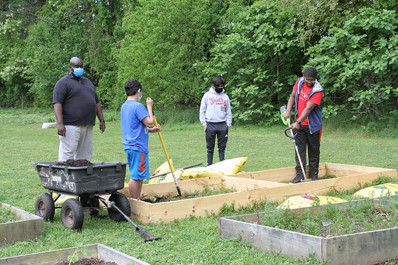 Michael Haynes, background left, and 23-year-old Thomas Langston, background right, observe as Robert Nyeing, 16, foreground left, and Emmanuel Joseph, 15, weed their raised bed before adding fresh garden soil and fertilizer. Haynes, Nyeing and Joseph are members of Corpus Christi Church, Stone Mountain. Langston is a member of Holy Cross Church, Atlanta. Photo By Michael Alexander