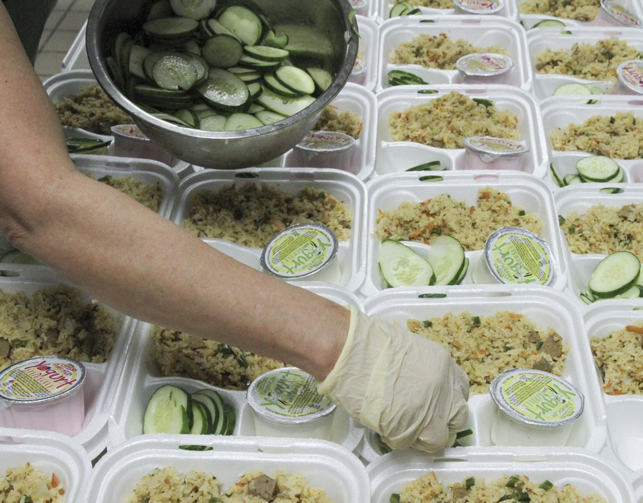 A volunteer places sliced cucumbers on the 500 plates being prepared for delivery to the homeless in the remote areas of three counties (Gwinnett, DeKalb and Fulton), encompassing more than 12 municipalities. Photo By Michael Alexander