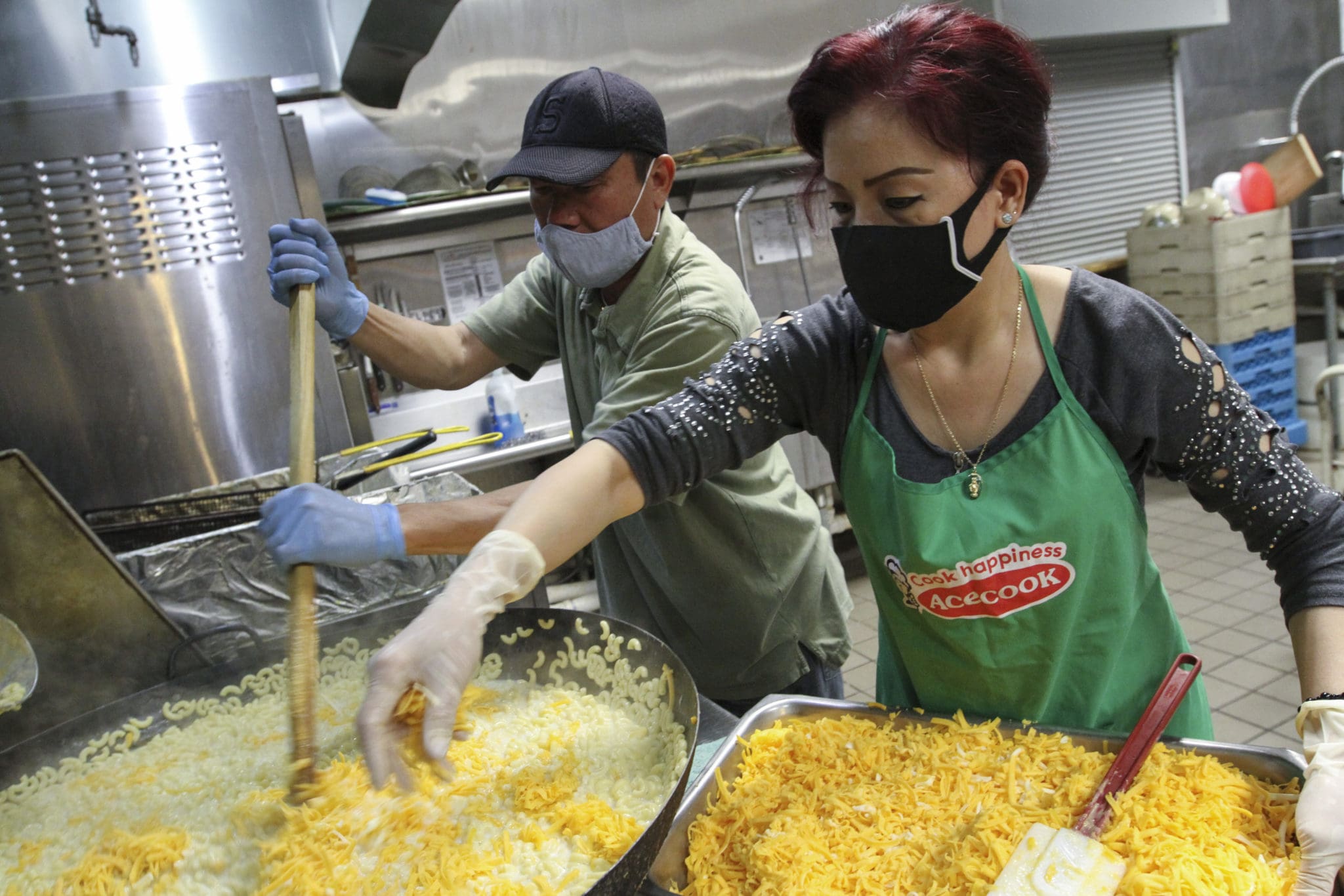 As Hoang Nguyen, left, stirs the noodles, Tam Ho sprinkles shredded cheese into the large pot. On Tuesdays, the main dish on the menu is either macaroni and cheese or spaghetti. Photo By Michael Alexander