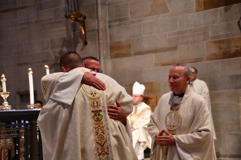 Father Neil Herlihy, right, pastor of St. Brigid Church, Johns Creek, looks on as Father Eric Hill, pastor of Prince of Peace Flowery Branch, embraces new priest Father Robbie Cotta. Father Herlihy and Father Hill were the vesting priests for Father Cotta at his June 12 ordination.
