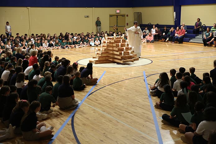After the monstrance was placed on the “burning bush” in the St. Catherine of Siena School gymnasium, Deacon Stephen Ponichtera, standing center, provides a brief reflection on the real presence of Jesus in the Eucharist. Photo By Michael Alexander