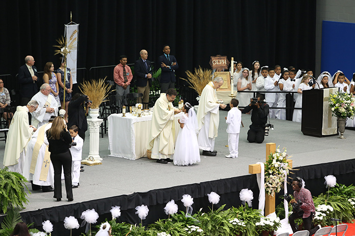 Father Rafael Carballo, left, the current pastor of Our Lady of Perpetual Help Church, Carrollton, and Father Richard Morrow, the founding pastor, distribute holy Communion to two of the 76 young people from the parish during a May 1 Mass at the University of West Georgia Coliseum. Photo by Michael Alexander