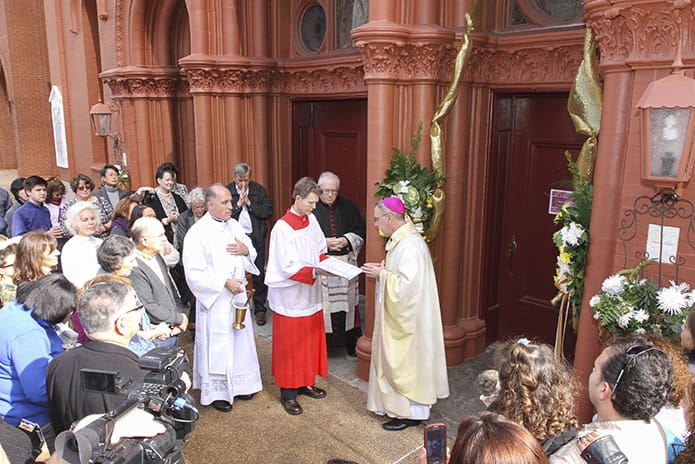 Sacred Heart of Jesus Basilica parishioner Jim Duryea holds the book as Bishop Luis Zarama conducts the rite for the opening of the Holy Door of Mercy. Looking on with the congregation is Msgr. Edward J. Thein, standing to Duryea’s left. Photo by Michael Alexander