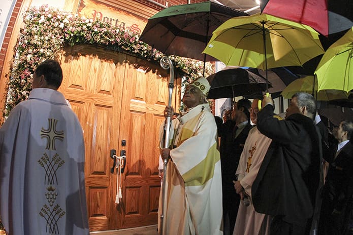 On an evening of pouring rain, Archbishop Wilton D. Gregory is shielded by umbrellas as he stands before the Holy Door of Mercy at the Holy Vietnamese Martyrs Church in Norcross. Photo By Michael Alexander