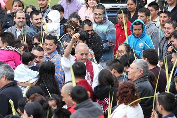 Father Fabio Alvarez Posada, center, pastor of St. Paul the Apostle Church, Cleveland, sprinkles the palms held by parishioners at St. Paul the Apostle Church, Cleveland, with holy water. Photo By Michael Alexander