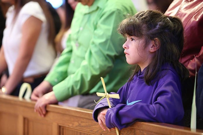 A little girl clings to her palm that was converted into a cross during the Palm Sunday Mass at St. Paul the Apostle Church, Cleveland. Photo By Michael Alexander