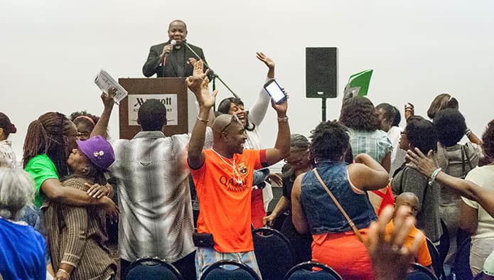 Participants in the Francophone track dance and sing to hymns of praise and worship during the first day of the 2016 Eucharistic Congress. Standing at the podium in the background is Father Cyprien Emile, the Francophone track speaker. Photo By Thomas Spink