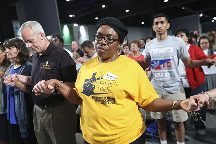 Anthonia Okonkwo, center, of St. John Vianney Church, Lithia Springs, joins hands with those on each side of her during the praying of the Our Father. Photo By Michael Alexander