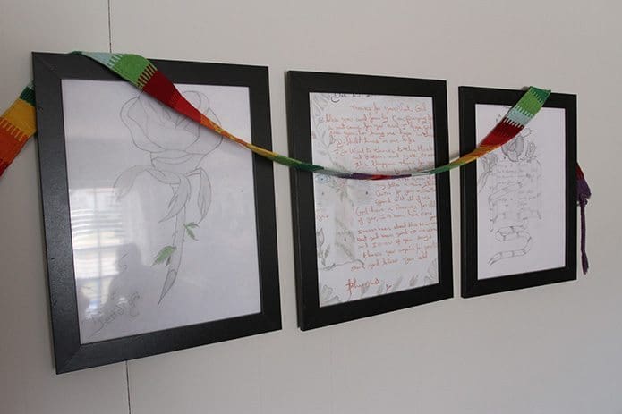 Artwork and a handwritten note of thanks from a detainee are displayed on a wall in the hospitality house’s living room. In the corner of the nearest drawing, written in Spanish are the words “Dios te bendiga” (God bless you). Photo By Michael Alexander