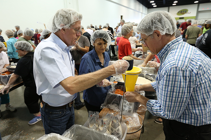 Michael Mead, left, of St. Peter Chanel Church, Roswell, pours in a cup of dehydrated soy, one of four items added to the meal bags, as Jim O’Connor, right, of the Shrine of the Immaculate Conception, Atlanta, holds the meal bag under the funnel. Irma Nanez, left center, of St. Philip Benizi Church, Jonesboro, waits to add a scoop of dehydrated vegetables. Photo By Michael Alexander