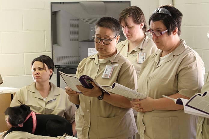 (L-r) Donna Porter, holding Hope, one of the dogs in the prison’s “Forever Friends” K9 Rescue Dog Program, Alma B. Mitchell, Amy Walden and Kim Consolino follow the Gospel reading during the May 6 Mass. Photo By Michael Alexander