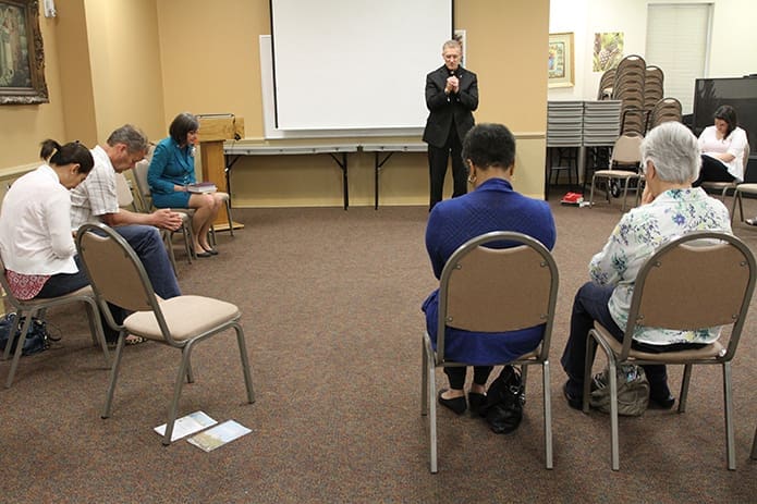 Deacon Leo Gahafer of St. Brigid Church, Johns Creek, conducts a closing prayer following the presentation by Mary Francis Bowley, background left, founder and chief strategy officer of Wellspring Living, a non-profit that helps to restore the lives of domestic sex trafficking victims. Photo By Michael Alexander