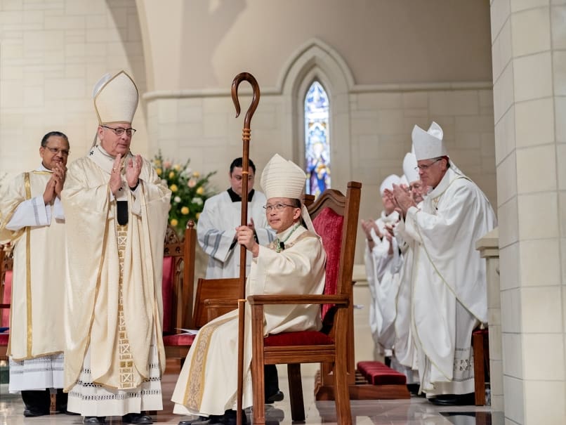 Archbishop Gregory J. Hartmayer, OFM Conv., at left, and other clergy members applaud Bishop John Nhan Tran, seated, following his ordination. Photo by Johnathon Kelso