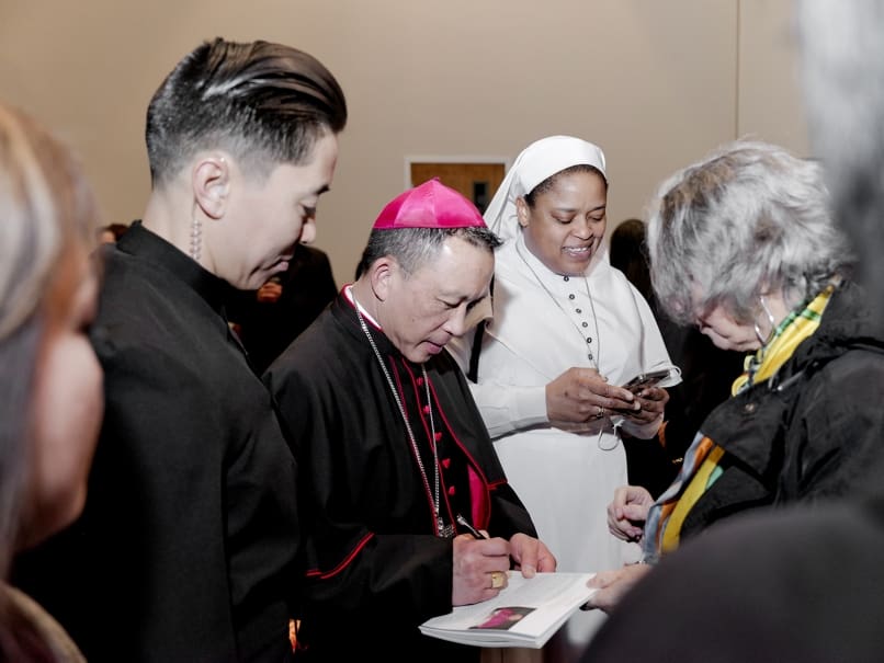 Bishop John Nhàn Tran signs a Mass program during a reception held following his episcopal ordination. Photo by Johnathon Kelso