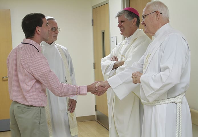 Just before the Oct. 2 Mass in the hospital chapel, Atlanta Veterans Administration Medical Center employee Bradley Hess shakes hands with Deacon Tom Badger of St. Ann Church, Marietta, as he also greets Bishop Ned Shlesinger. Standing next to Hess is hospital chaplain Father John Kieran. Photo By Michael Alexander