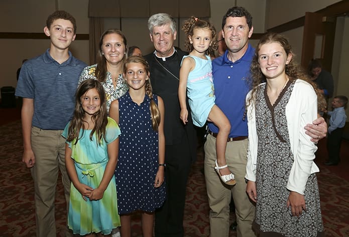 During the reception that followed the vespers service, Bishop-designate Bernard E. (Ned) Shlesinger III, center, poses for a photo with (clockwise, starting third from right) Leah Smith, 3-years-old, her father Anthony, her sister Rachel, 17, her sister Sarah, 13, her sister Rebekah 9-years-old, her brother Luke, 15, and her mother Tracy. When he was a parish priest, Bishop-designate Shlesinger officiated Anthony and Tracy’s July 12, 1997 wedding at St. Mary Church, Wilmington, N.C. Today they attend St. Mark Church in Wilmington. Photo By Michael Alexander