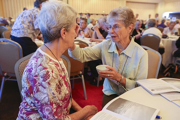 Just before the “chains of bondage” were broken, each person at their table administered the sign of the cross to their neighbor with holy water. It was a solemn moment of forgiveness and reconciliation for any discrimination or hurt afflicted upon a person of color. Here Sisters of the Holy Family Marietta Fahey of Freemont, Calif., right, signs the forehead of Religious Sisters of Charity Madeleine Meagher of San Pedro, Calif. Photo By Michael Alexander