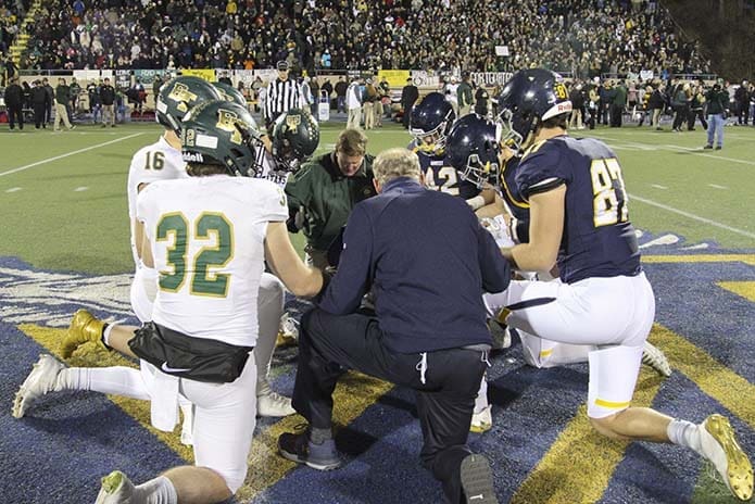 After the coin toss and prior to kickoff, Marist School athletic director Tommy Marshall, back to camera, and Blessed Trinity High School athletic director Ricky Turner, facing Marshall, take a knee with the team captains as they all pray the Our Father at midfield. Photo By Michael Alexander