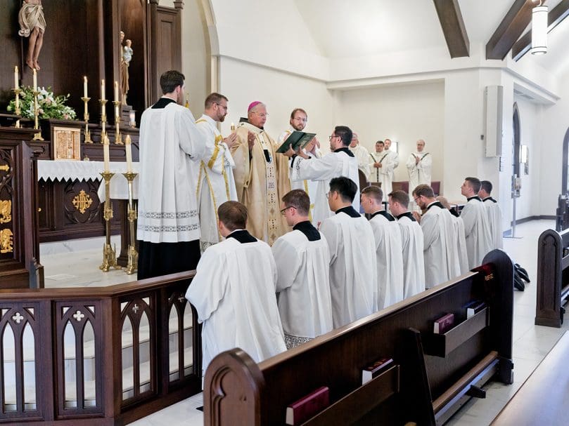 Nine seminarians kneel at the altar as Archbishop Gregory J. Hartmayer, OFM Conv., reads from the Roman Pontifical during the candidacy Mass at Christ the Redeemer Church July 27. Photo by Johnathon Kelso