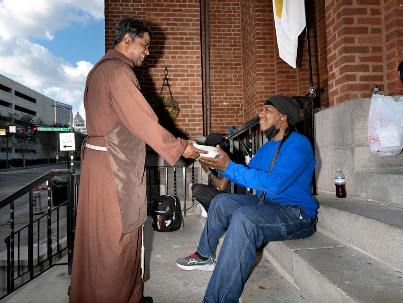 Capuchin Franciscan Brother Praveen Turaka brings a meal from the food truck to a man in need outside the Shrine of the Immaculate Conception. Photo by Johnathon Kelso