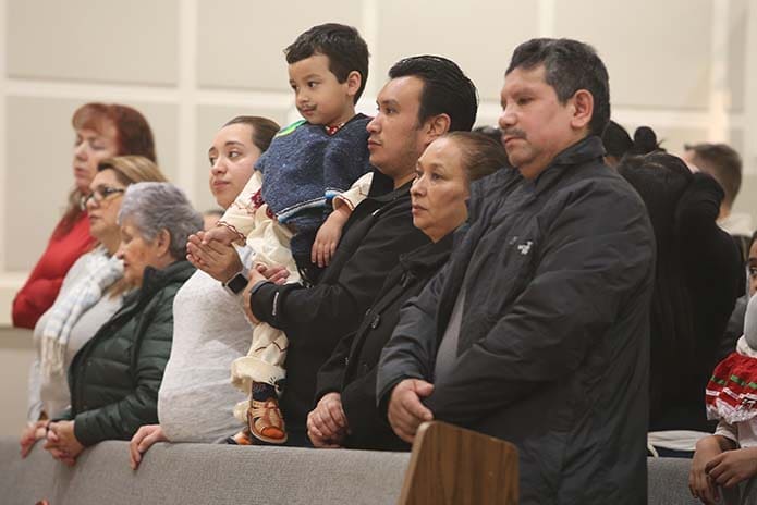 Standing with the congregation at Divino Niño Jesús Mission, Duluth, during the intercessory prayers, two-year-old Camilo Reyes holds the hand of his mother, Estrella, as he is held by his father David. Also joining them on the pew are Camilo’s grandparents, Augustin, far right, Luz Maria. Photo By Michael Alexander