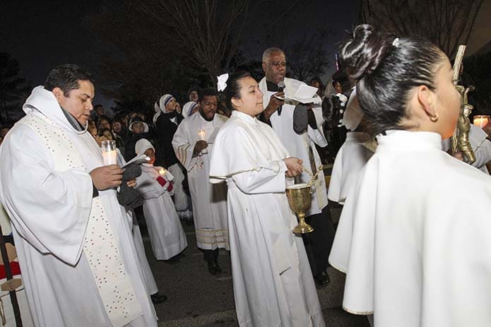 Father Jacques Fabre, background, right center, administrator of San Felipe de Jesús Mission in Forest Park, leads a prayer before the procession in honor of Our Lady of Guadalupe sets off from the grounds of the mission to streets around the community. Photo By Michael Alexander