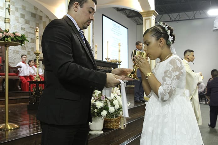 Eugenio Velazquez, left, presents the Blood of Christ to Naomy Jimenez, one of over 80 children who made their first Holy Communion during two separate Masses at the mission on May 19. Photo By Michael Alexander