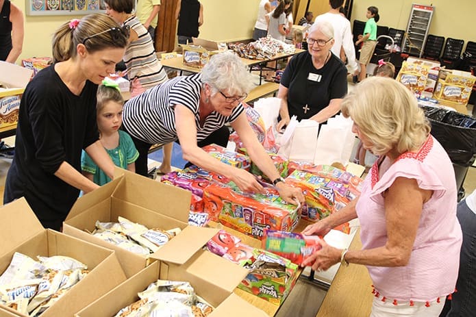 From the end of the table, second from the right, Carol Hunt, a Cathedral of Christ the King member and a longtime MUST Ministries volunteer, observes participants unpack and sort juice boxes. Hunt, a former teacher, started the MUST Ministriesâ summer lunch program in 1995. Photo By Michael Alexander
