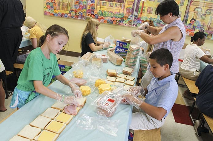((Counter clockwise, from left) Kate Dowhy, 8, Isaac Coronado, 11, and his mother Tere participate in a July 13 sandwich preparation project in the Cathedral of Christ the King parish school cafeteria. The sandwiches are given to MUST Ministries for its summer lunch program, where volunteers distribute them during the months schools are on summer break to the children who are eligible to receive a free or reduced lunch during the school year. Photo By Michael Alexander