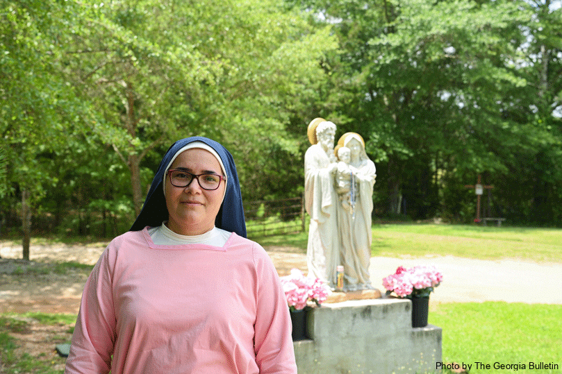 Sister Irina, a consecrated hermit, stands in the shade on a hot summer's day in front of the entrance to her home, neighboring the Our Loving Mother’s Children retreat center in Conyers. The sun shines on a statue of the Holy Family behind her.  Photo by Julianna Leopold
