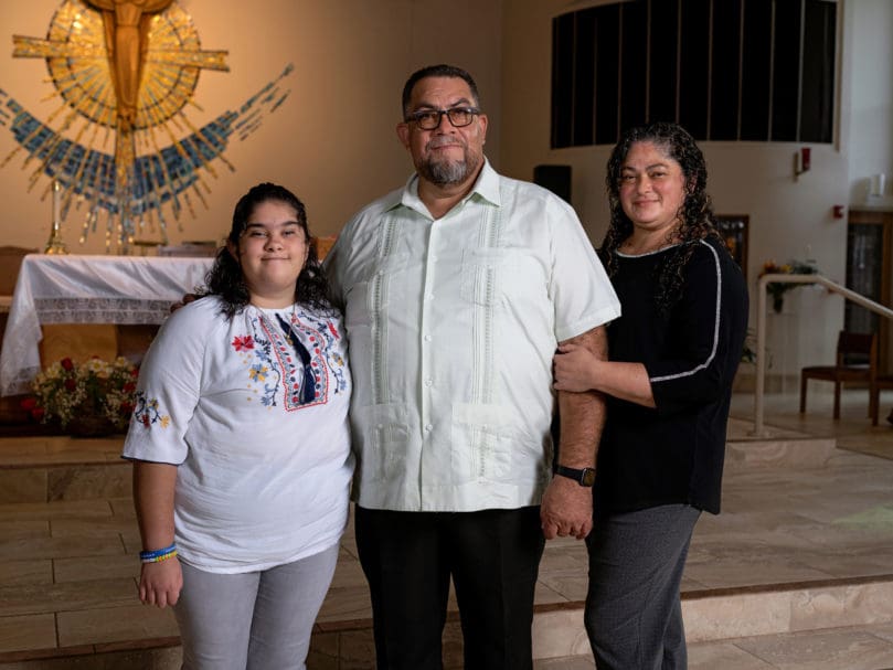 Hector Villanueva, center, stands near the altar with his wife Lourdes, right, and his daughter Bernadette, left, at Corpus Christi Church. They joined other parishioners to mark the church's 50th anniversary this month. Photo by Johnathon Kelso