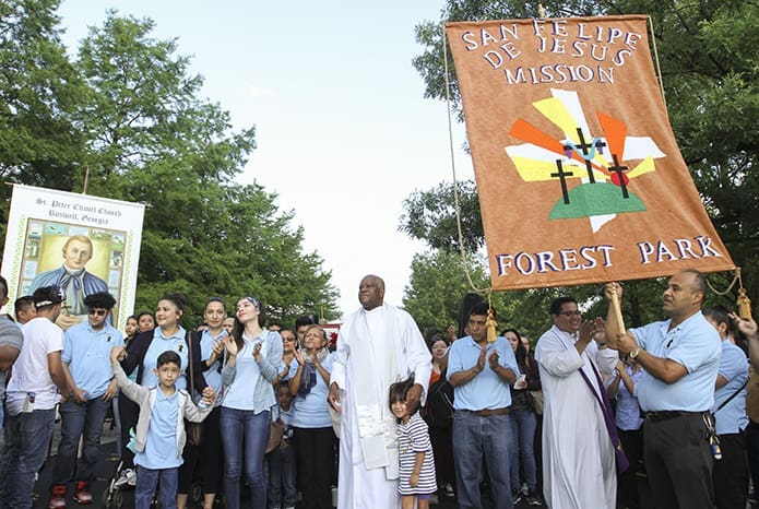 Prior to the morning procession, Scalabrinian Father Jacques Fabre, center, administrator of San Felipe de Jesús Mission in Forest Park, joins his parishioners as they praise God with the members of Sacred Heart of Jesus Church, Hartwell, who led the singing and music. Photo By Michael Alexander
