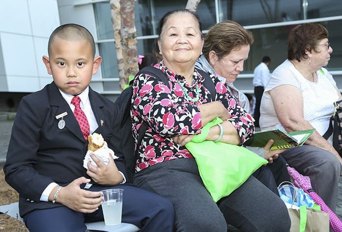 Raphael Le, left, grabs a bite to eat at the conclusion of the Eucharistic Congress, while he and his grandmother Anne Truong, second from left, a member of St. Joseph Church, Marietta, wait for the bus to pick up their party. Le, who attends the Cathedral of Christ the King, Atlanta, made his first holy Communion on May 12 of this year. Photo By Michael Alexander