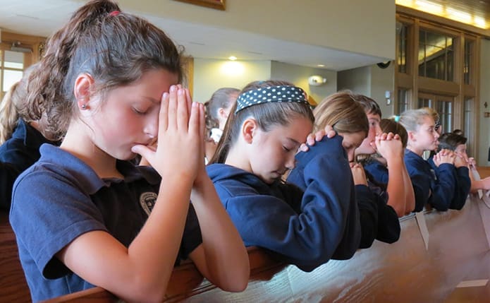 Father Neil Dhabliwala, pastor of St. Catherine of Siena Church, Kennesaw, led the prayer service for peace on Friday, Sept. 9 with students like eighth-graders Reagan Bentley, left, and Abigail Hohl at SCS School. Singing was led by Teri Khan and the Angel Choir. The preschool children and faculty joined the elementary school community for the service. Photo By Vinita John