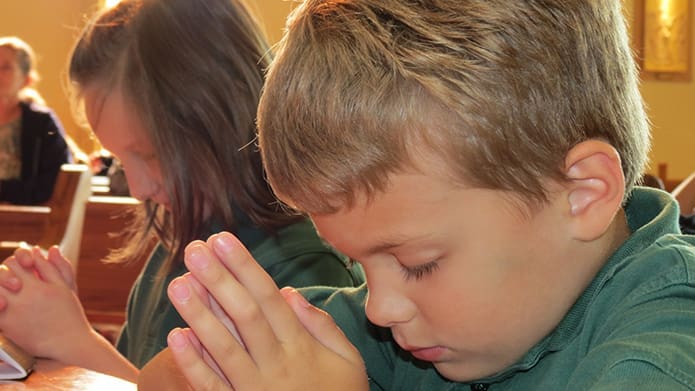 St. Catherine of Siena School's Gus Gamull, foreground, and Elizabeth Adrian pray with their fellow students during a prayer service for peace. Photo By Vinita John