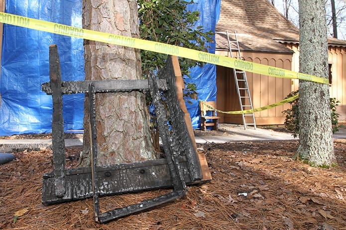 A burnt piece of furniture rests against a tree as a tarp covers the side of the Roswell church where it incurred damage from an arson fire. Photo By Michael Alexander
