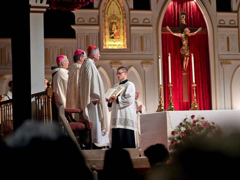 A seminarian of the Archdiocese of Atlanta holds the missal while Cardinal Blase Cupich, forefront, Archbishop Christophe Pierre, and Archbishop Gregory J. Hartmayer, OFM Conv., background, sing the responsorial psalm during the closing Mass of the 25th Eucharistic Congress. Photo by Johnathon Kelso