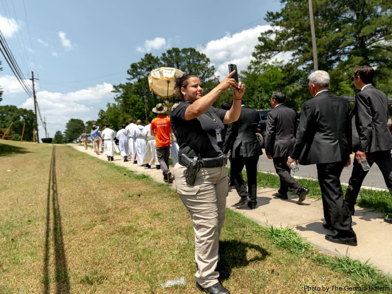 A police officer looks on as the eucharistic procession passes through the streets of Riverdale on the way to Our Lady of Vietnam Church. Photo by Johnathon Kelso