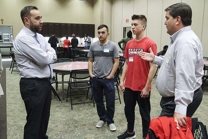 (R-l) Gary Armstrong and his sons Brian, 16, and Jack, 17, chat with Family Promise of Gwinnett County executive director, Matt Elder, during a pre-Christmas event for Family Promise families in St. Augustine Hall at St. Monica Church, Duluth. Armstrong and his family have volunteered with the parish Family Promise ministry for four years. Photo By Michael Alexander