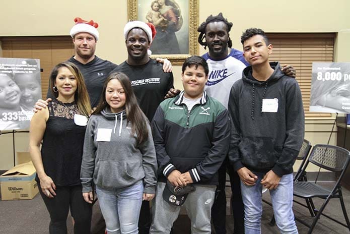 (Back row, l-r) Brooks Reed, defensive end and linebackers Sean Weatherspoon and De’Vondre Campbell of the Atlanta Falcons pose for a photo with (front row, l-r) Della Carbajal and her children Sky, Angel and Jacob, during a Dec. 19 pre-Christmas event for Family Promise families in St. Augustine Hall at St. Monica Church, Duluth. The Carbajals are volunteers with the parish Family Promise ministry. Photo By Michael Alexander