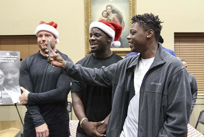 Fifteen-year-old Sharod Doll takes a selfie with (background, l-r) Brooks Reed, defensive end and linebacker Sean Weatherspoon of the Atlanta Falcons. Doll was one of the Family Promise of Gwinnett County clients residing at St. Monica Church, Duluth, who participated in a Dec. 19 pre-Christmas function for Family Promise families in the parish’s St. Augustine Hall. Photo By Michael Alexander