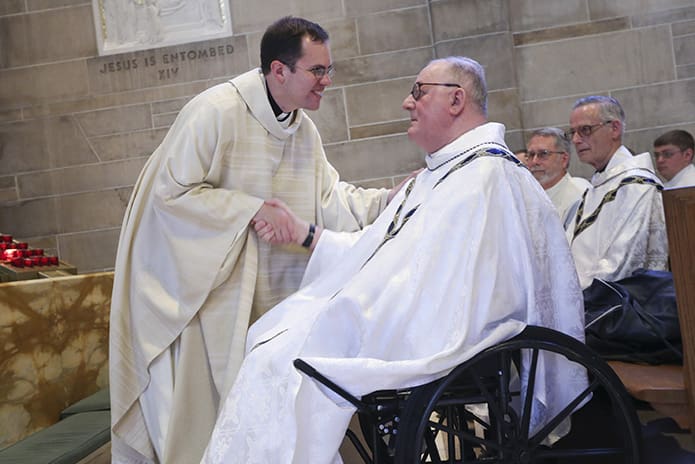 In an unprecedented gesture during the ordination last year, the new priests, including Father Brian Bufford, left, walked over to the side aisle to extend the presbyteral greeting of peace to Father Richard Kieran, a senior priest who also observed his 50th priestly anniversary in 2015. Photo By Michael Alexander