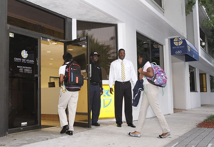 Just after 7 a.m. Patrick Medley, second from right, dean of discipline at Cristo Rey Atlanta Jesuit High School, Atlanta, welcomes students and security officer Daintez Jackson, second from left, holds the door open as they enter the West Peachtree Street entrance. The school year and business training institute began Aug. 4. Photo By Michael Alexander