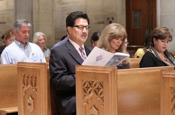 Dr. Carlos Franco, foreground left, and his wife Mabel of St. Brigid Church, Johns Creek, follow along in singing the offertory hymn. Dr. Franco is a doctor of hematology and oncology. Photo By Michael Alexander