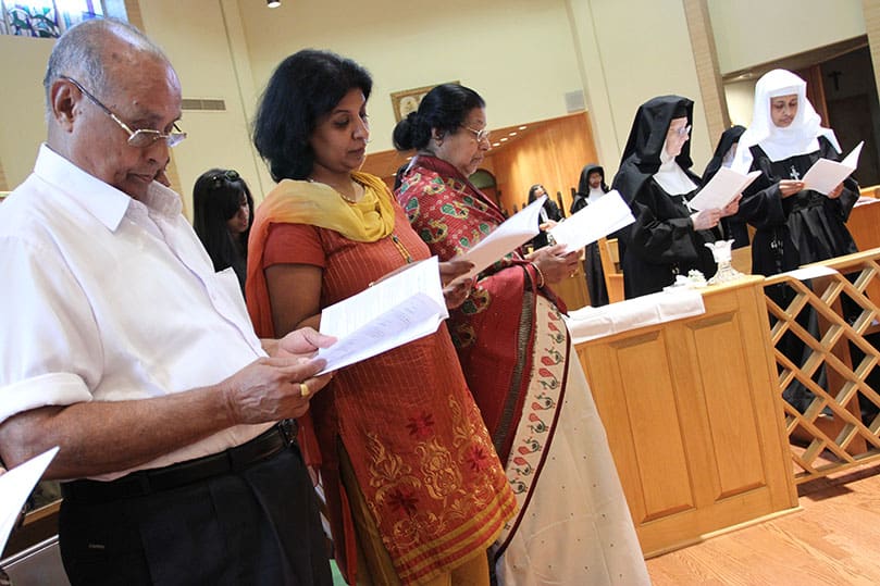 As Archbishop Gregory recites the solemn consecration of the professed, (l-r) Sister Teresa Maria's uncle Jacob Pullappally of Illinois, her sister Stella Stephen of Michigan and her mother Aleyamma Kulangara of New York follow along in their programs. Photo By Michael Alexander
