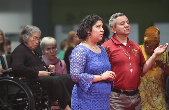 Stephanie Toole, center, a member of St. Peter’s Catholic Church, Columbia, S.C., and Jose Duarte of Immaculate Heart of Mary Church, Atlanta, pray before the Blessed Sacrament with hundreds of other people. Photo By Michael Alexander